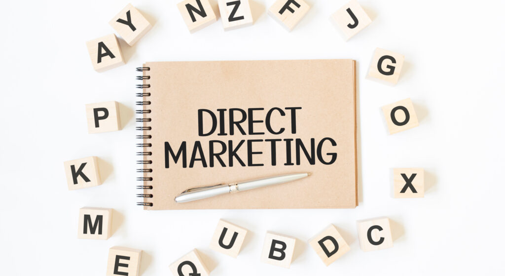 Direct marketing written on a notebook with pen surrounded by different alphabets.